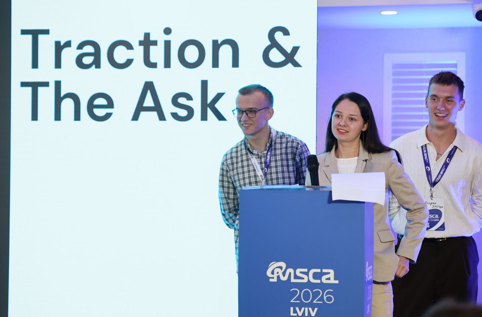 Three young founders at the lectern presenting a slide titled Traction and The Ask